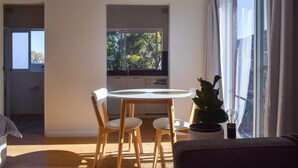 Ein modernes Wohnzimmer mit einem runden Esstisch, zwei weißen Stühlen, einem Topf mit Pflanze und einem großen Fenster mit Vorhängen.