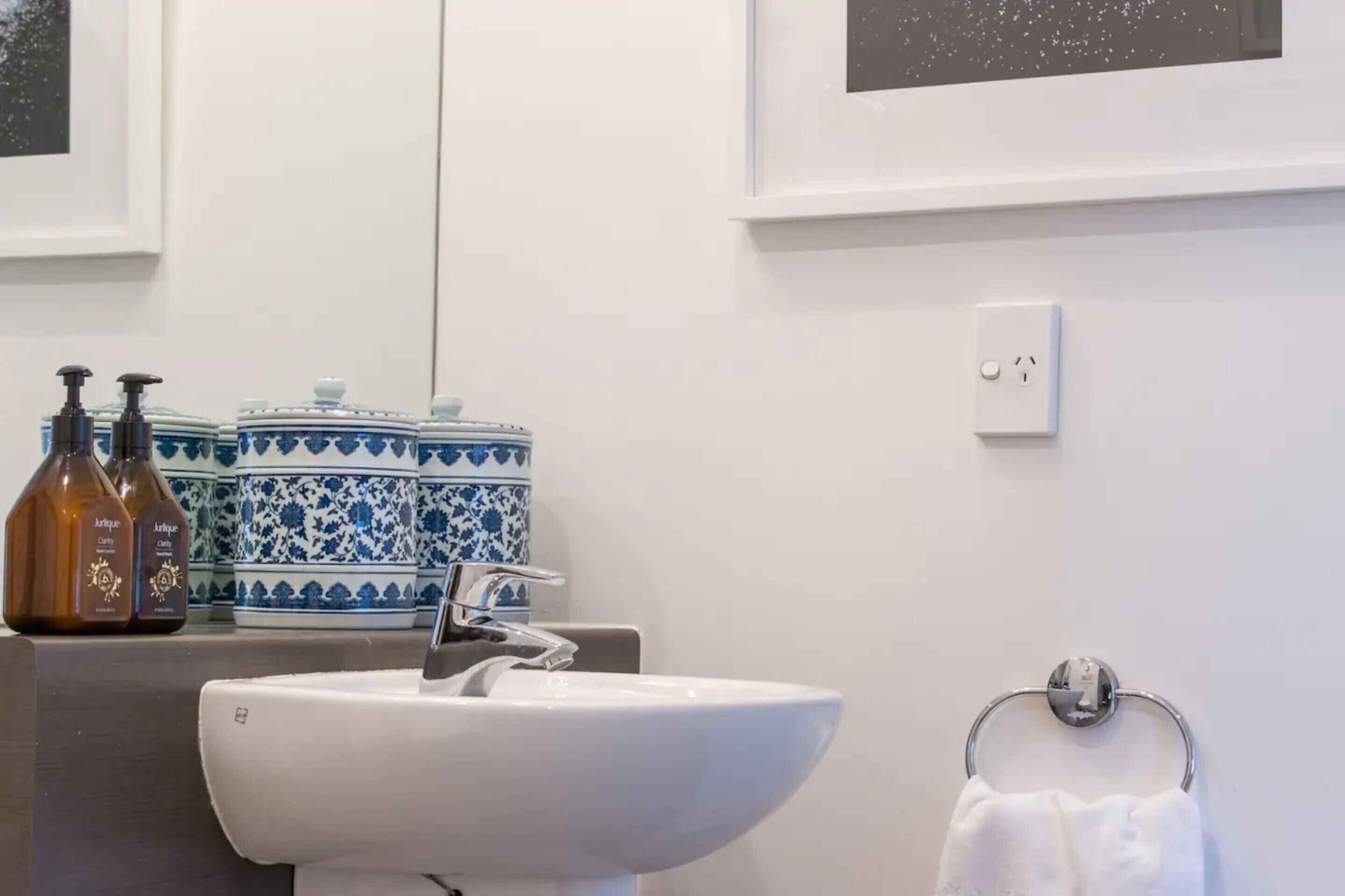 Un baño con lavamanos blanco, un perchero y recipientes de cerámica azul y blanca decorativos.