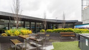 An outdoor area with a modern building, benches, and planters with yellow flowers. - Modern 1 Bedroom in Tranquil Parklands (Parkville)