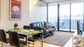 A modern living room with a glass table, black leather sofa, and a cityscape poster. - Modern 1 Bedroom in Tranquil Parklands (Parkville)