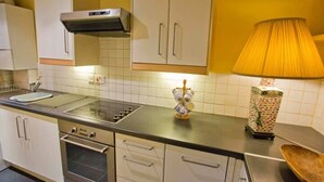 Une cuisine avec des armoires blanches, une cuisinière, un four et un four à micro-ondes. Une lampe se trouve sur le plan de travail.