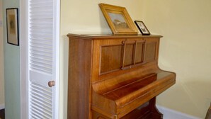 Un piano en bois, surmonté d’un cadre photo, se trouve dans un coin d’une pièce dotée d’une porte et d’un mur de couleur claire.