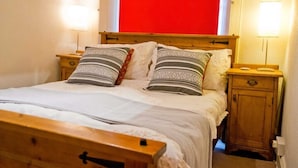 Un lit avec une tête de lit en bois, deux tables de chevet avec des lampes et un mur rouge derrière le lit.