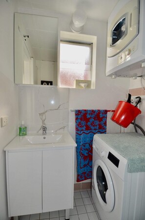 A compact bathroom with a white sink, a washing machine, and a red bucket. - Cute Studio Apartment in Maroubra (Maroubra)