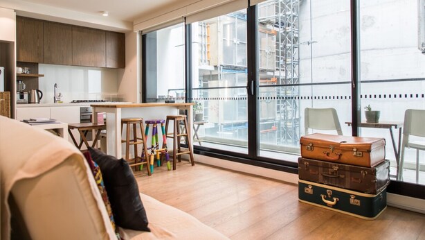 Una cocina moderna con armarios de madera, un comedor con mesa y sillas, y ventanas amplias que ofrecen vistas de la ciudad.