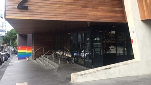 Un edificio moderno con un gran letrero con el número 2, una escalera que lleva a la entrada y una bandera arcoíris en la pared.