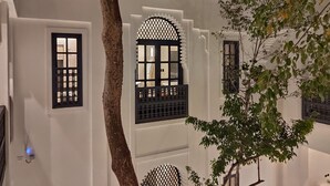 Ein traditionelles Gebäude mit weißen Wänden und schwarzen Fenstergittern, im Vordergrund steht ein Baum.