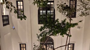 Ein weißes Gebäude mit vielen Fenstern und einem Baum im Vordergrund.