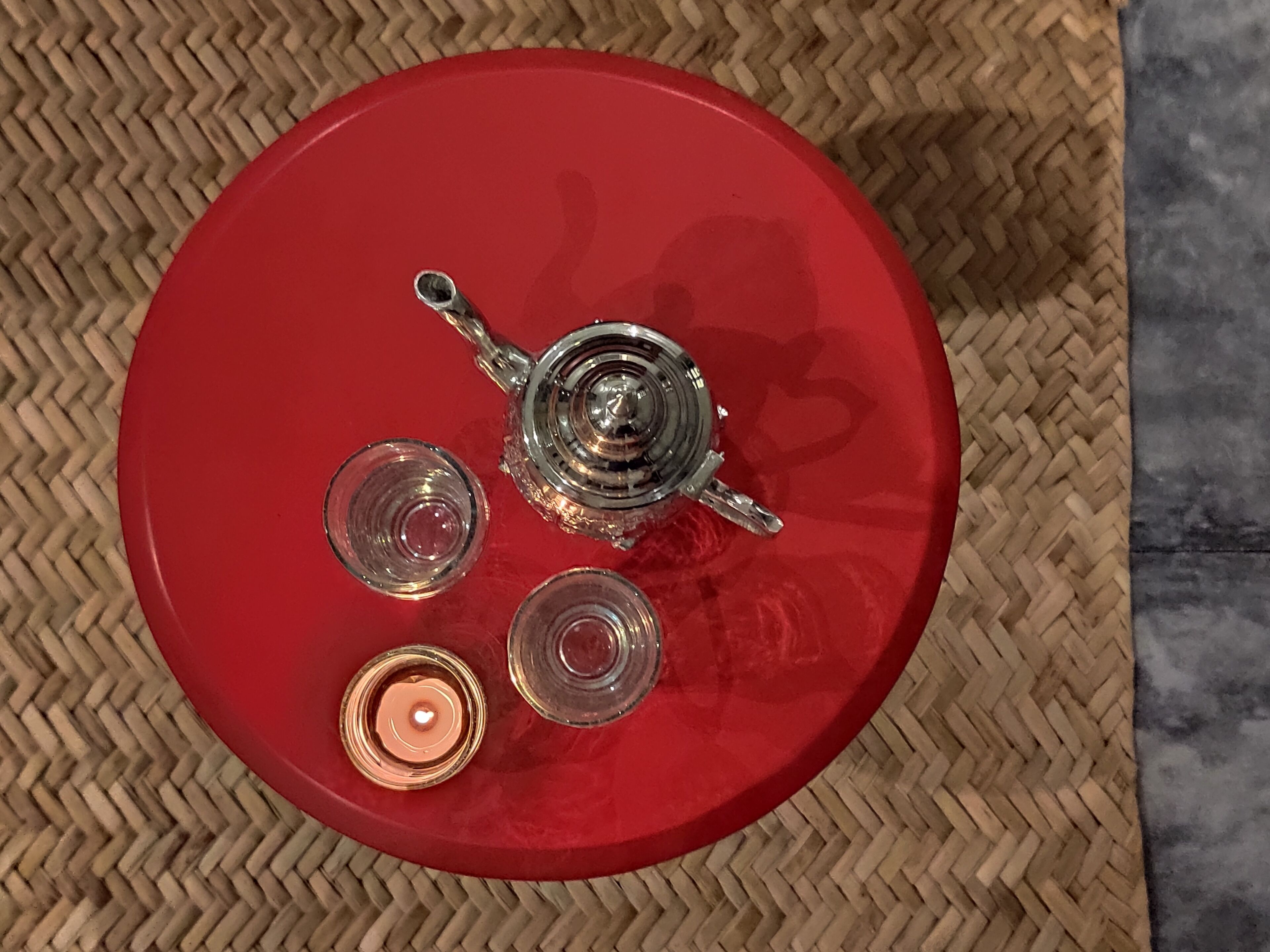 Une table rouge avec une théière, trois verres et une bougie.