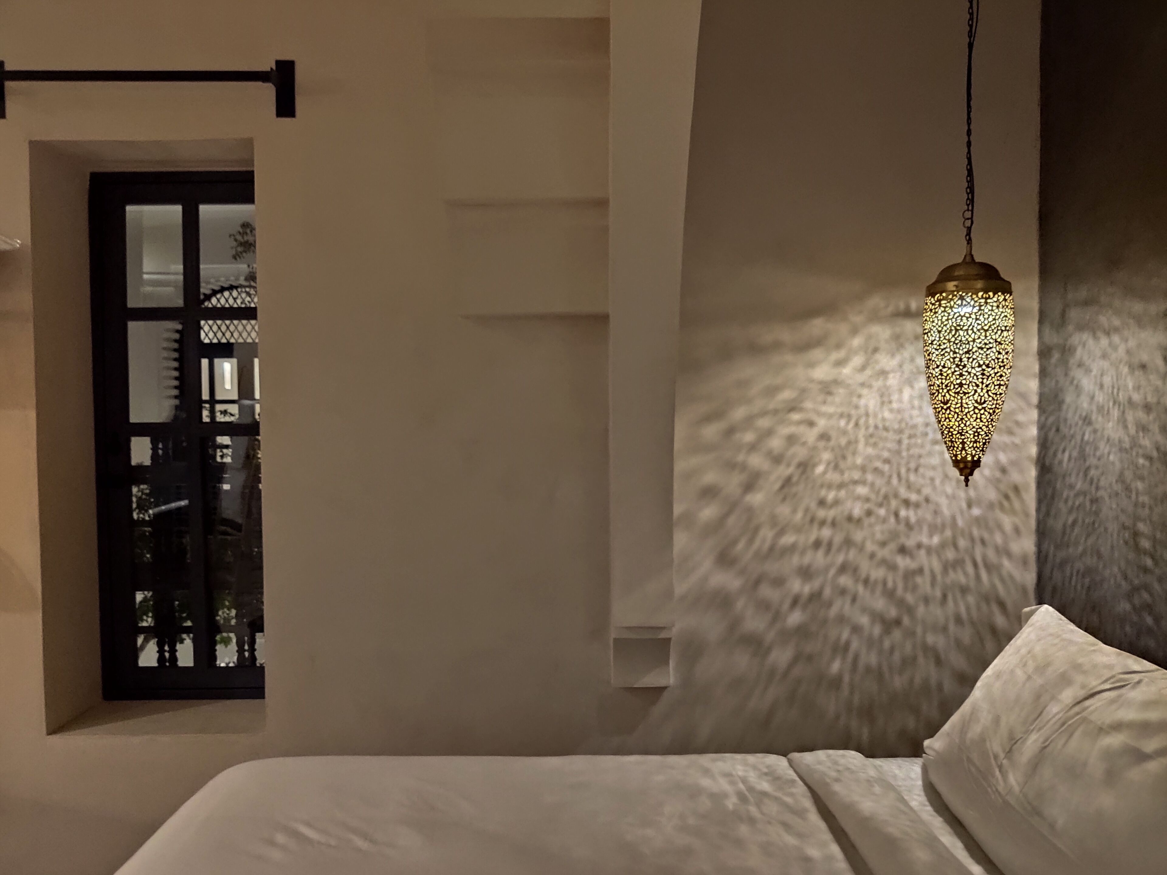 Ein Schlafzimmer mit einem Bett, einer Hängelampe und einem Fenster mit Blick auf ein Gebäude.