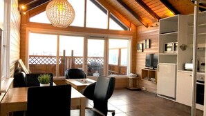 A cozy kitchen with a dining area, wooden beams, large windows, and a hanging light fixture. - Vacation Home Fagravik (Akureyri)