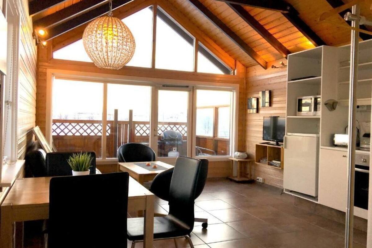 Une cuisine chaleureuse avec un coin repas, des poutres en bois, de grandes fenêtres et un luminaire suspendu.