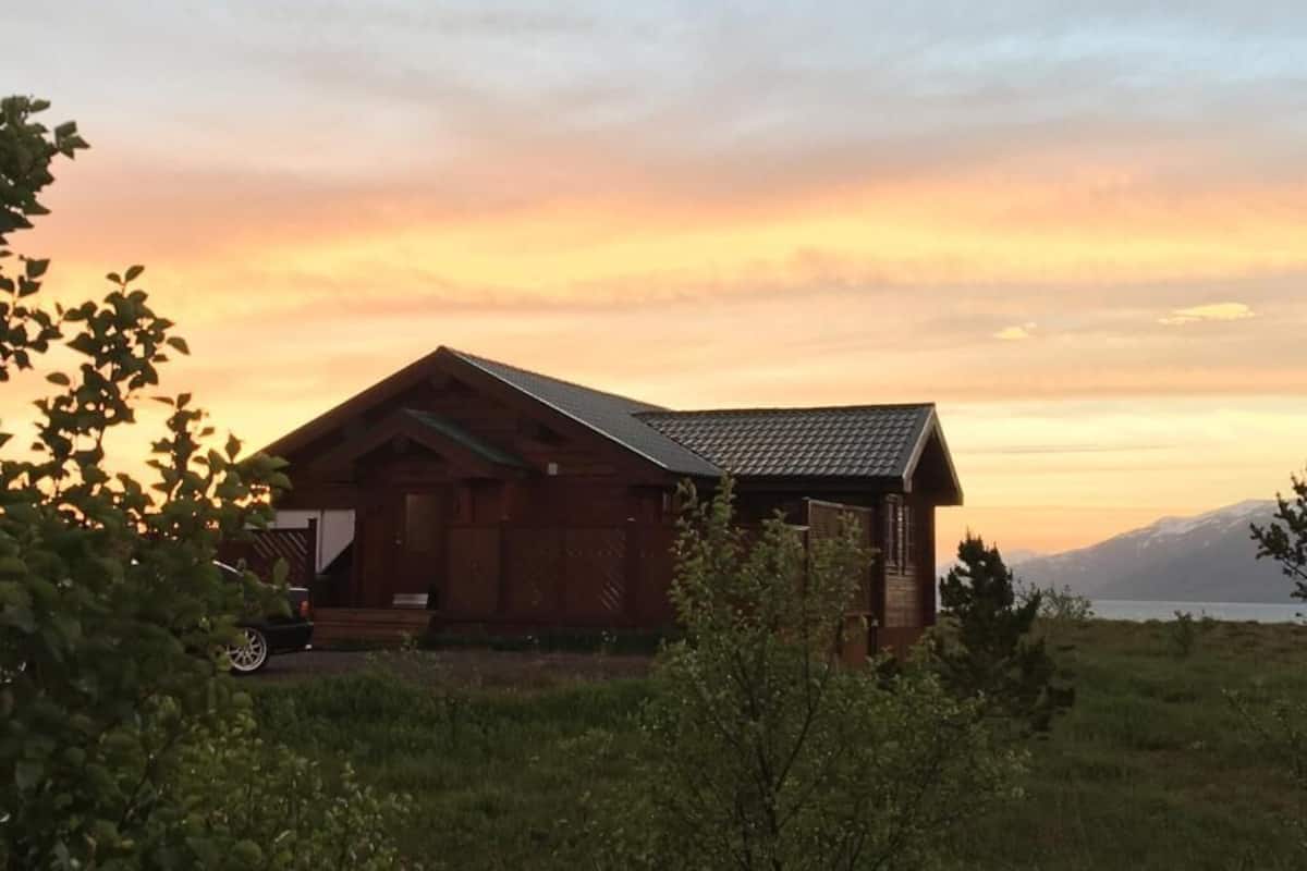 Une cabane en bois, dotée d’un toit en pente, située dans un champ verdoyant et offrant une vue sur les montagnes au loin.