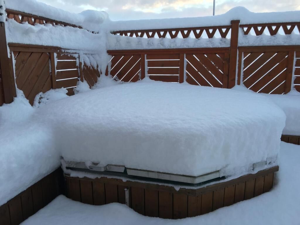 A snow-covered outdoor hot tub surrounded by wooden fencing.