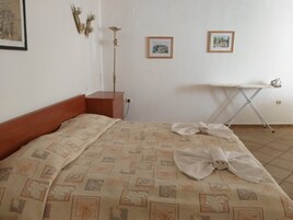Una cama bien tendida con una colcha estampada, una mesita de noche de madera, una lámpara de pie y dos cuadros enmarcados en la pared.