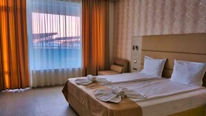 Une chambre d’hôtel avec un grand lit, un fauteuil de massage et une vue dégagée à travers des rideaux transparents.