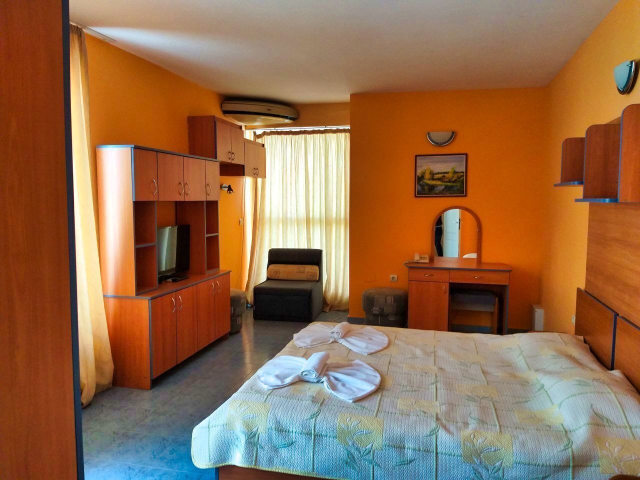 A hotel room with a bed, a TV, a desk, a chair, and a wardrobe.