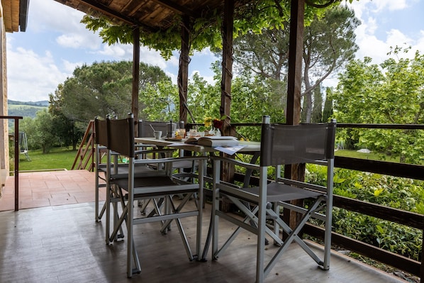 An outdoor dining area with metal tables and chairs, surrounded by a wooden fence and lush greenery.