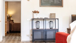 Una habitación con una cama, un escritorio con dos lámparas de malla negra, un jarrón blanco con flores secas y un menú en una pizarra que enumera productos orgánicos.