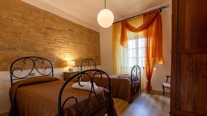 Una habitación con dos camas, una pared de ladrillo, una puerta de madera y una ventana con cortinas naranjas.