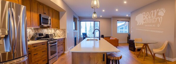 A modern kitchen with stainless steel appliances, a large island, and a dining area with a glass table and chairs.