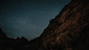 A starry night sky above a rocky landscape with a tent-like structure at the base. - Wadi Rum Bedouin B&B Malakot (Al-Quwayrah)