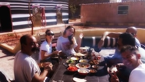 A group of people seated around a table with various dishes, suggesting a communal meal setting. - Wadi Rum Bedouin B&B Malakot (Al-Quwayrah)