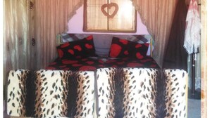 A bed with a heart-shaped window, a patterned bedspread, and a curtain backdrop. - Wadi Rum Bedouin B&B Malakot (Al-Quwayrah)