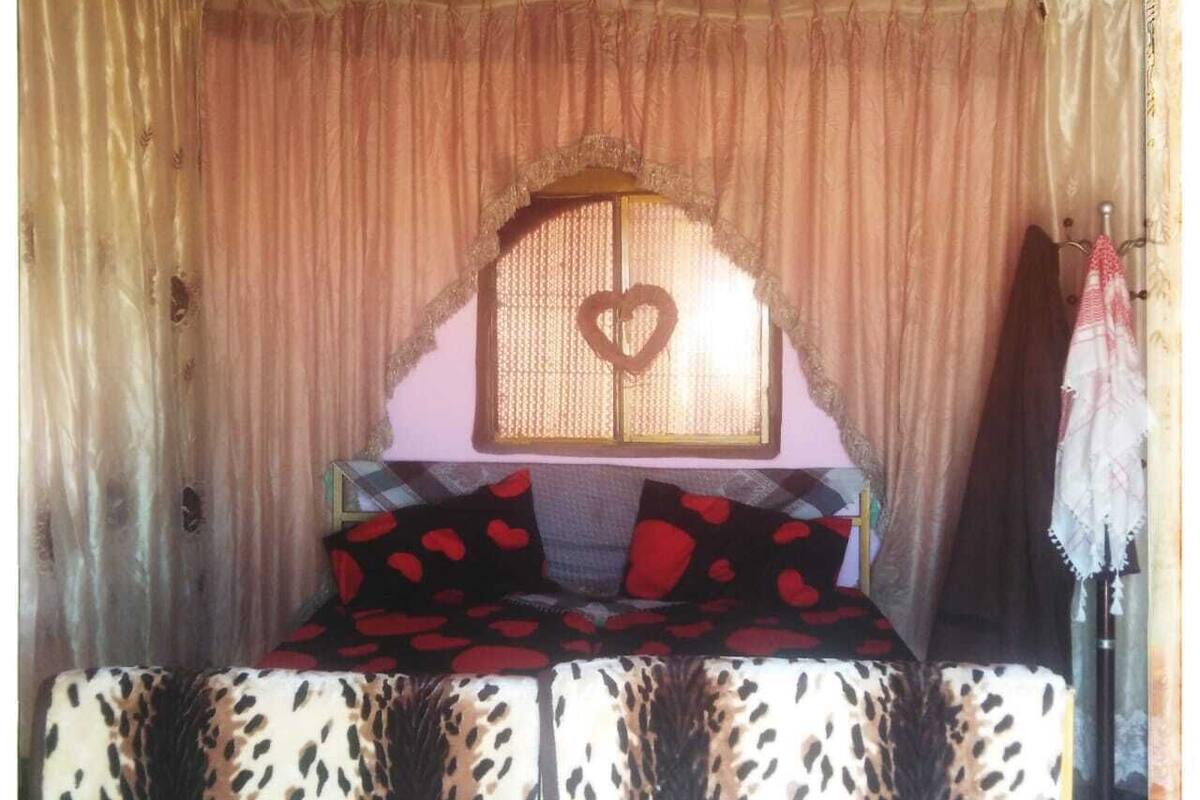 A bed with a heart-shaped window, a patterned bedspread, and a curtain backdrop.