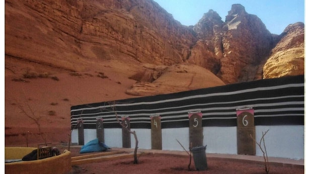 A desert landscape with a building featuring numbered columns and a striped wall. - Wadi Rum Bedouin B&B Malakot (Al-Quwayrah)