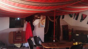 A dining area with a table and chairs, a hanging red cloth, and a wall with a map and flags. - Wadi Rum Bedouin B&B Malakot (Al-Quwayrah)