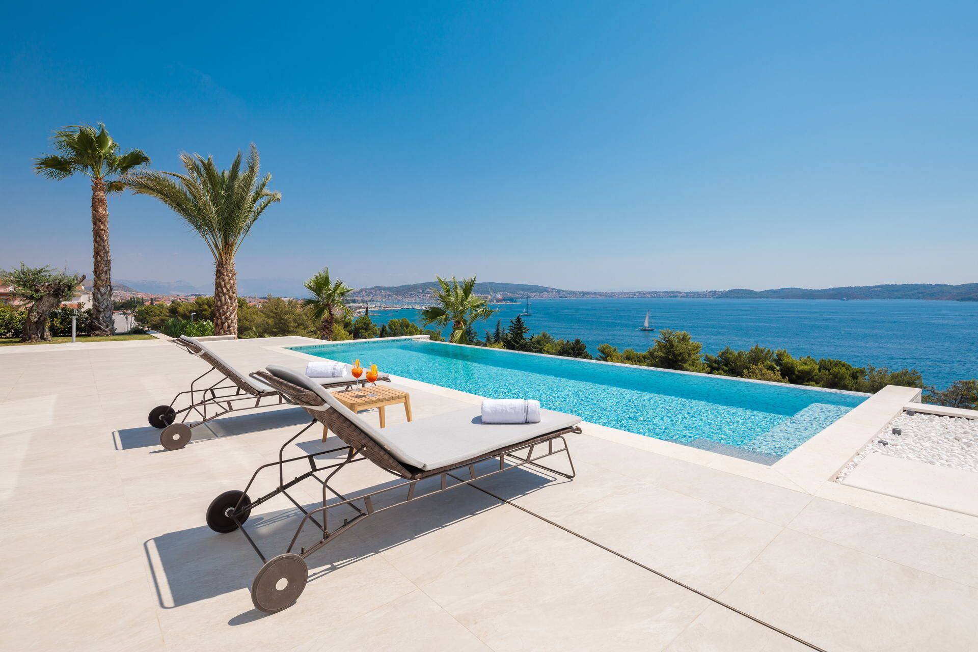Ein Poolbereich mit Liegestühlen, einem kleinen Tisch mit Getränken und Blick aufs Meer.