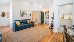 Una sala moderna con un sofá azul, piso de madera y una escalera que lleva a una zona de cocina.