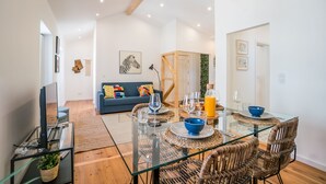 Un salon moderne avec une table à manger en verre, des chaises en osier, un canapé bleu et un téléviseur posé sur un meuble en verre.