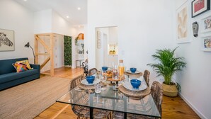 Un salon moderne avec une table à manger au plateau en verre, des chaises en osier et un canapé bleu.