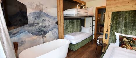 A modern hotel room with a large bathtub, bunk beds, a painting of a mountain, and a green textured wall.