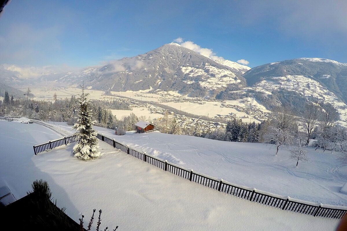 A snowy landscape with a mountain in the background, a fenced area, and a small building.