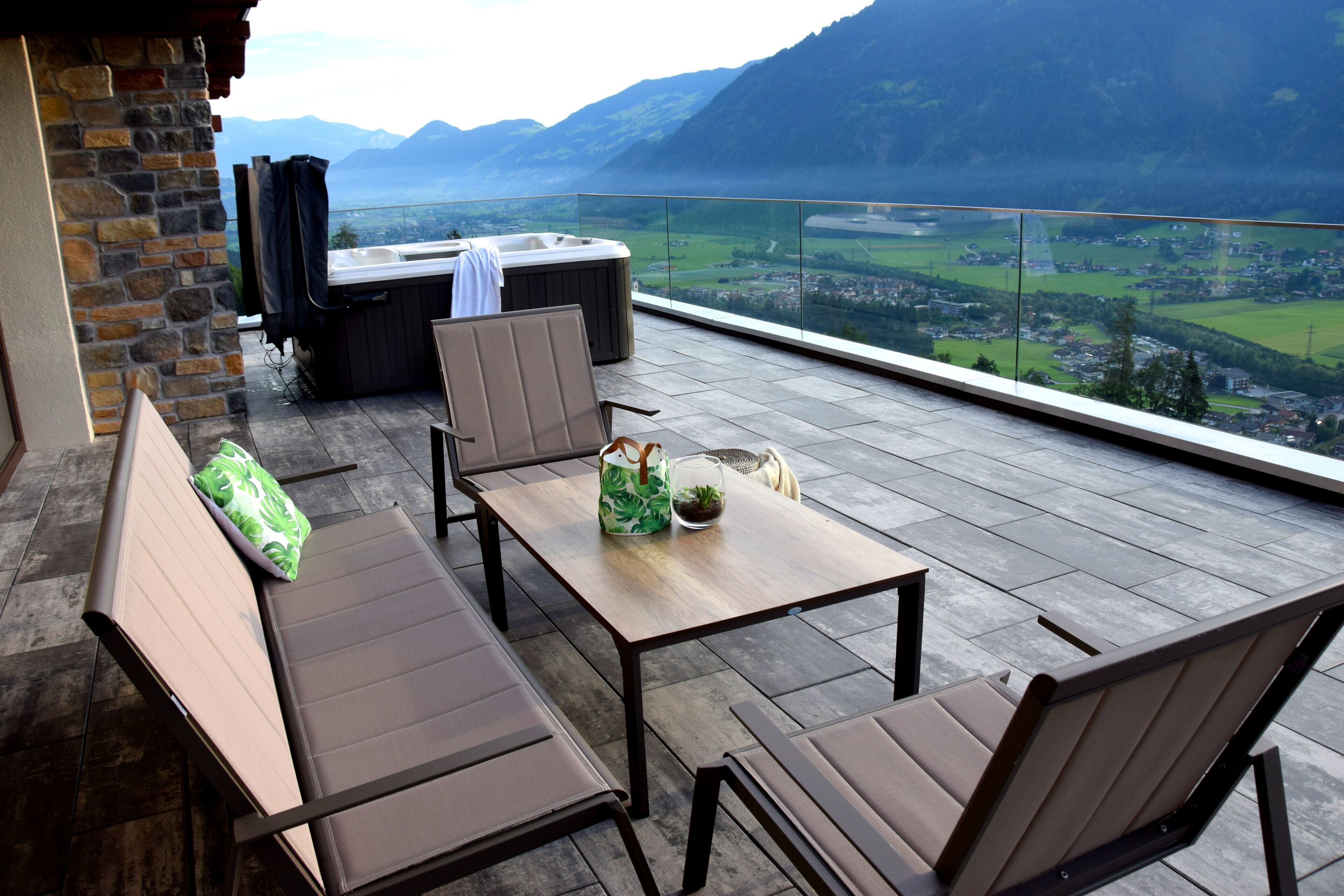 A terrace with a wooden table and chairs, a hot tub, and a view of a valley.