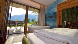 A bedroom with a large bed, a bathtub, and a sliding glass door leading to an outdoor area with a table and chairs. - Deluxe Suite Goldreh - SKI in/SKI out, Sauna-Jacuzzi - by "wachterhof" (Kaltenbach)