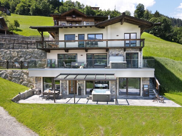 Ein modernes, zweistöckiges Haus mit Naturstein-Fassade, großen Fenstern und einem Balkon mit Sitzgelegenheit.