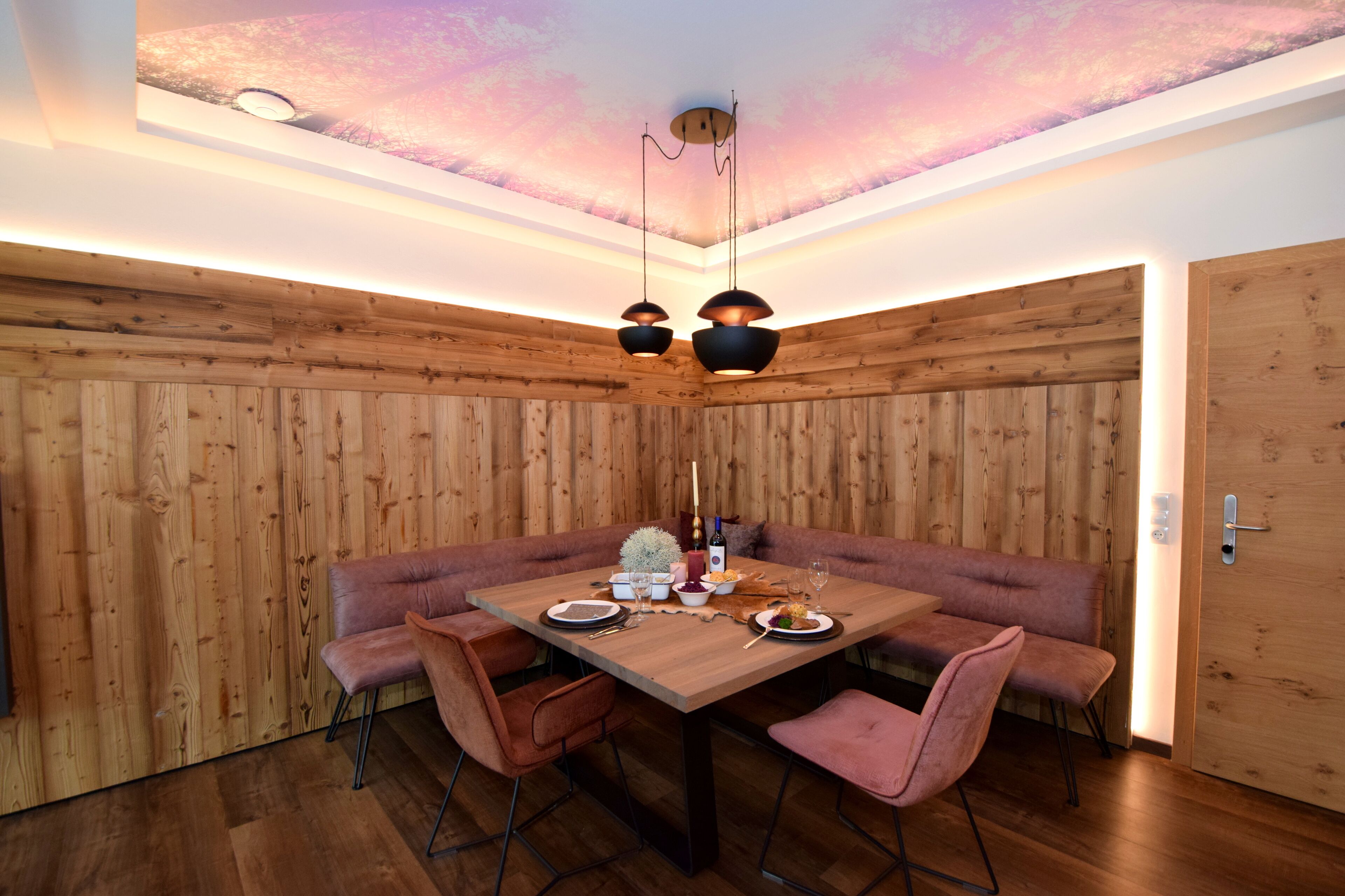 A dining area with a wooden table and benches, a ceiling with a painted design, and pendant lighting.