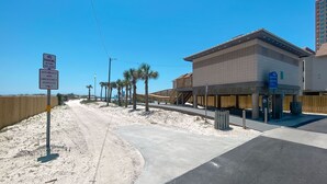 A building with a sandy beach in the background, a no parking sign, and a wooden fence. - Paradise Isle 34- ACROSS FROM BEACH, OUTDOOR POOL, GREAT PRICE! (Gulf Shores)