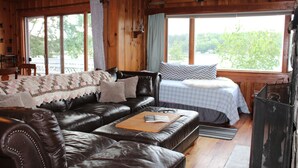 A cozy room with a leather sofa, a wooden coffee table, and a bed with a blue checkered bedspread. - Waterfront House on Winnipesaukee w Private Dock , Sleeps 11 & Dogs Welcome! (Moultonborough)
