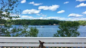 A wooden deck with a bench overlooking a lake, surrounded by trees and a clear sky. - Waterfront House on Winnipesaukee w Private Dock , Sleeps 11 & Dogs Welcome! (Moultonborough)