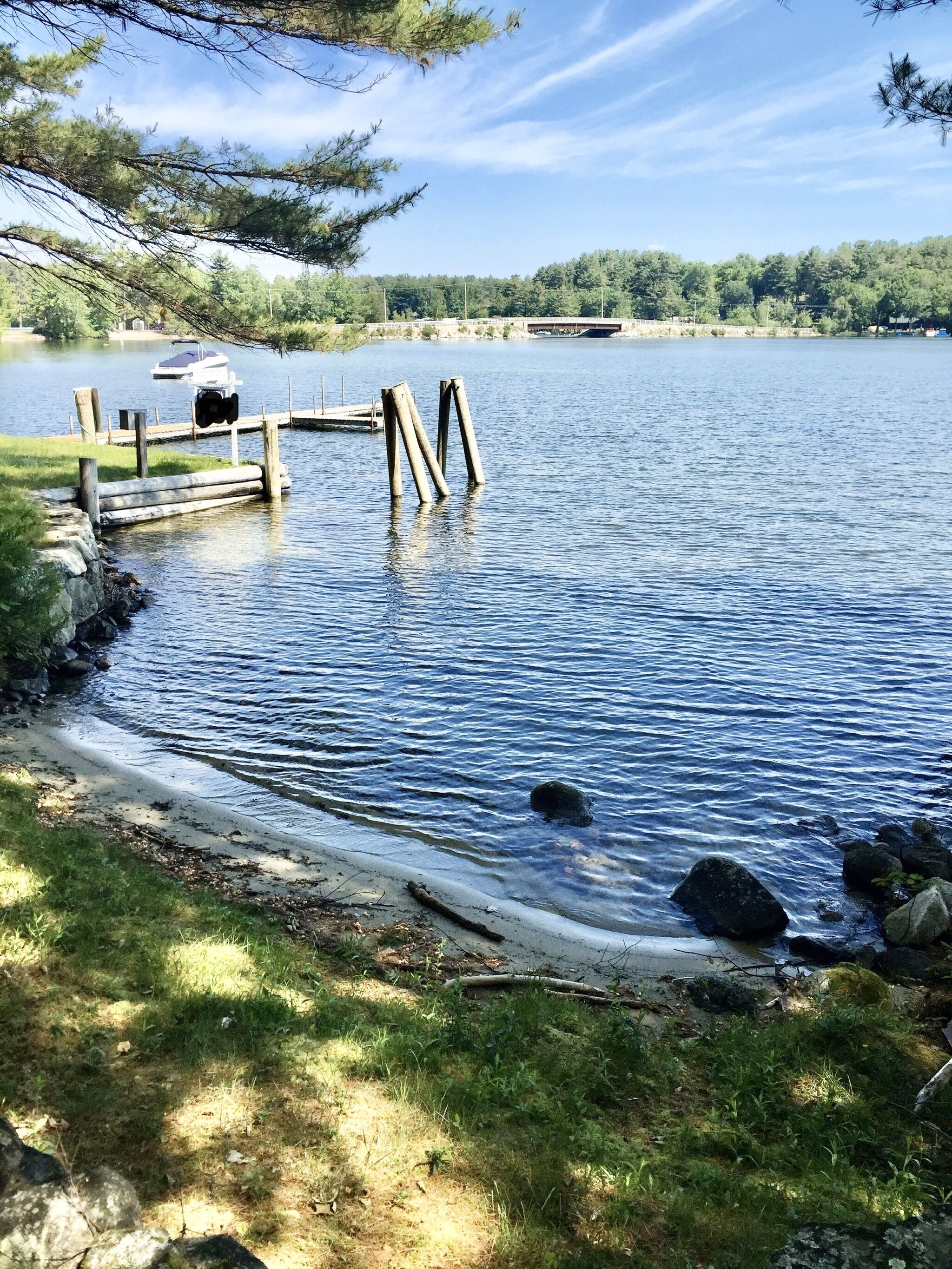 Un quai au bord du lac, avec un bateau amarré, entouré de verdure et d’arbres.