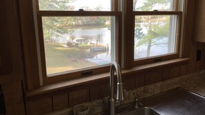 A kitchen with a stainless steel sink, wooden cabinets, and a window overlooking a backyard with a pond. - Waterfront House on Winnipesaukee w Private Dock , Sleeps 11 & Dogs Welcome! (Moultonborough)