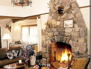 Uma sala de estar acolhedora com lareira de pedra, um sofá confortável e uma mesa de centro com diversos objetos.