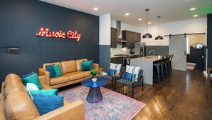 Ett modernt vardagsrum med en brun lädersoffa, blå och gröna kuddar, ett runt soffbord med en växt och en neonskylt med texten "Music City".