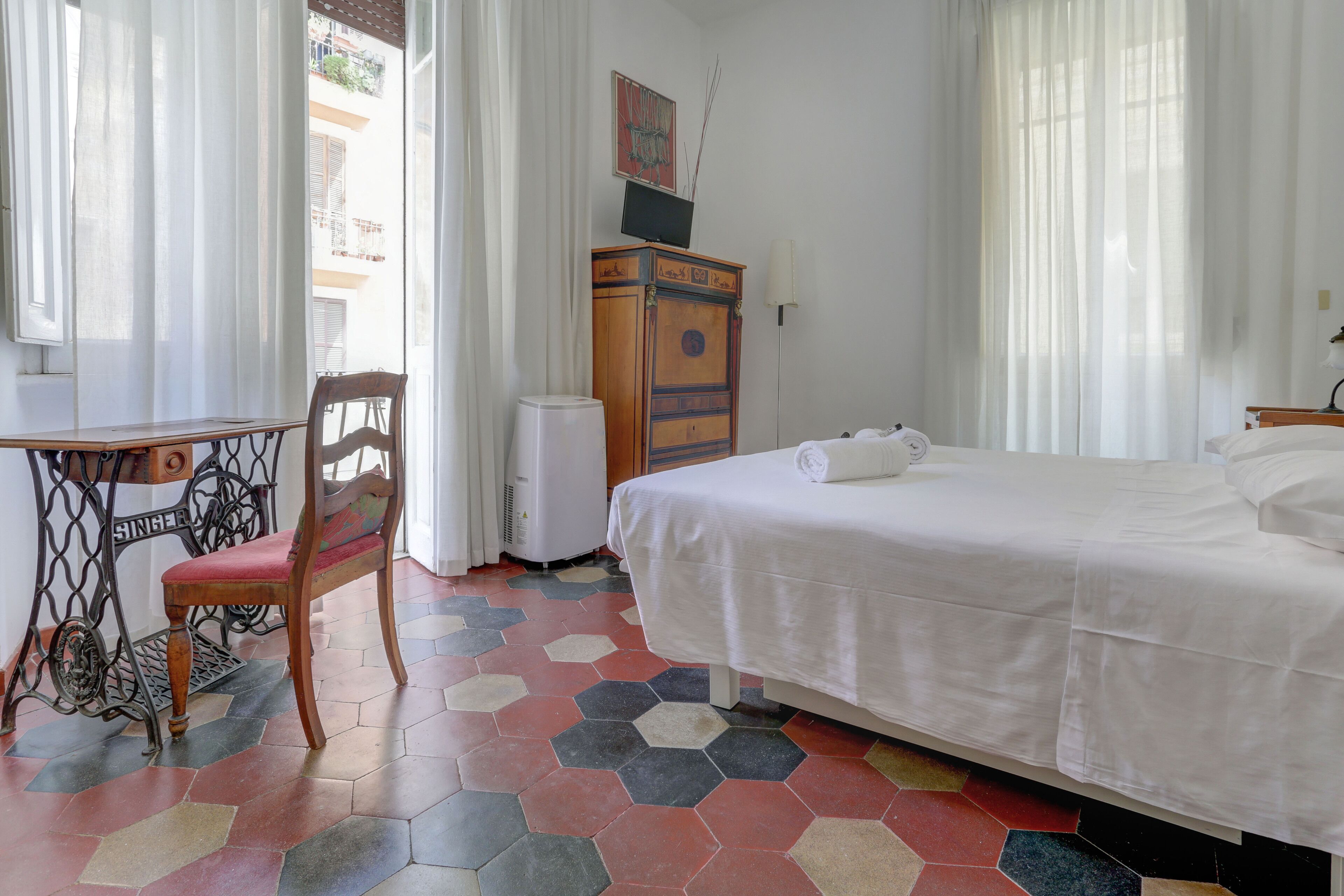 Une chambre d’hôtel avec un lit, un bureau, une chaise, une armoire et un radiateur.