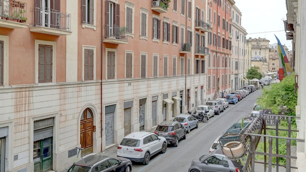 A row of parked cars along a narrow street lined with multi-story buildings with balconies and shutters. - Charming Colosseum (Rome)